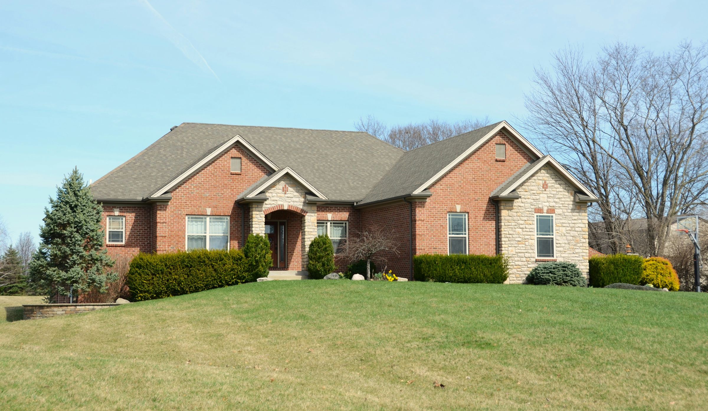 Single-story brick and stone home with a wide green lawn